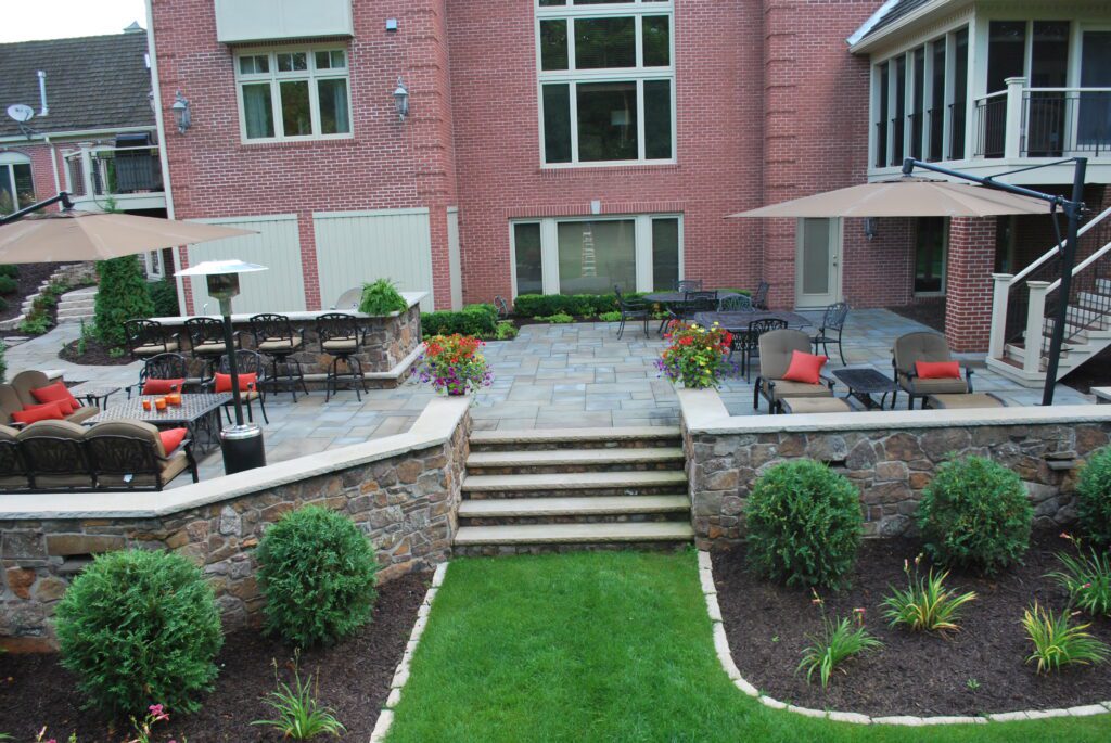 Multi-level bluestone patio featuring custom stacked stone retaining walls, patio steps, and a built-in outdoor bar - Yellow Brick Road Pavers & Landscapes LLC