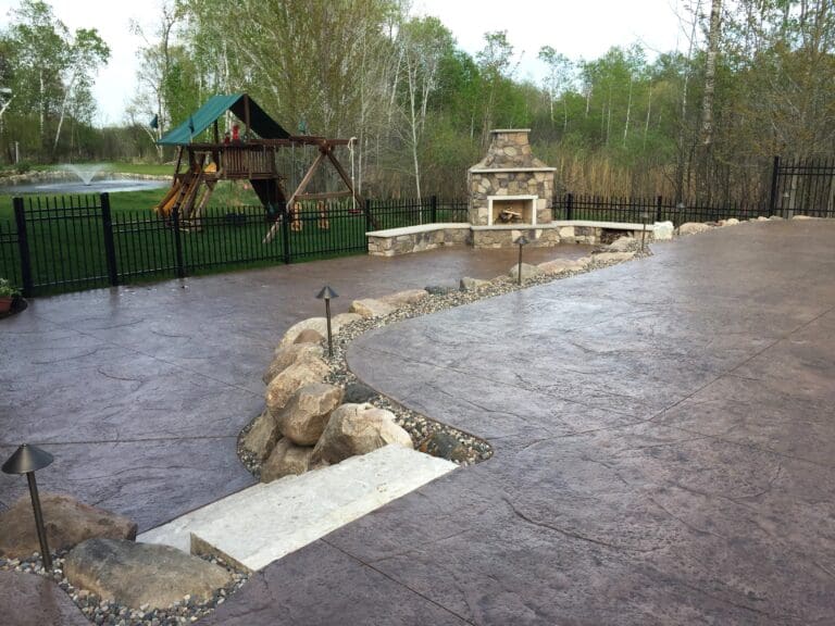 Large stamped concrete patio featuring a custom outdoor stone fireplace with built-in wood storage and curved seat walls - Yellow Brick Road Pavers & Landscapes LLC