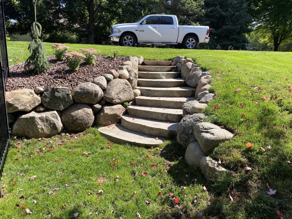exterior of a home with a custom rock retaining wall and stone steps - Yellow Brick Road Pavers & Landscapes LLC