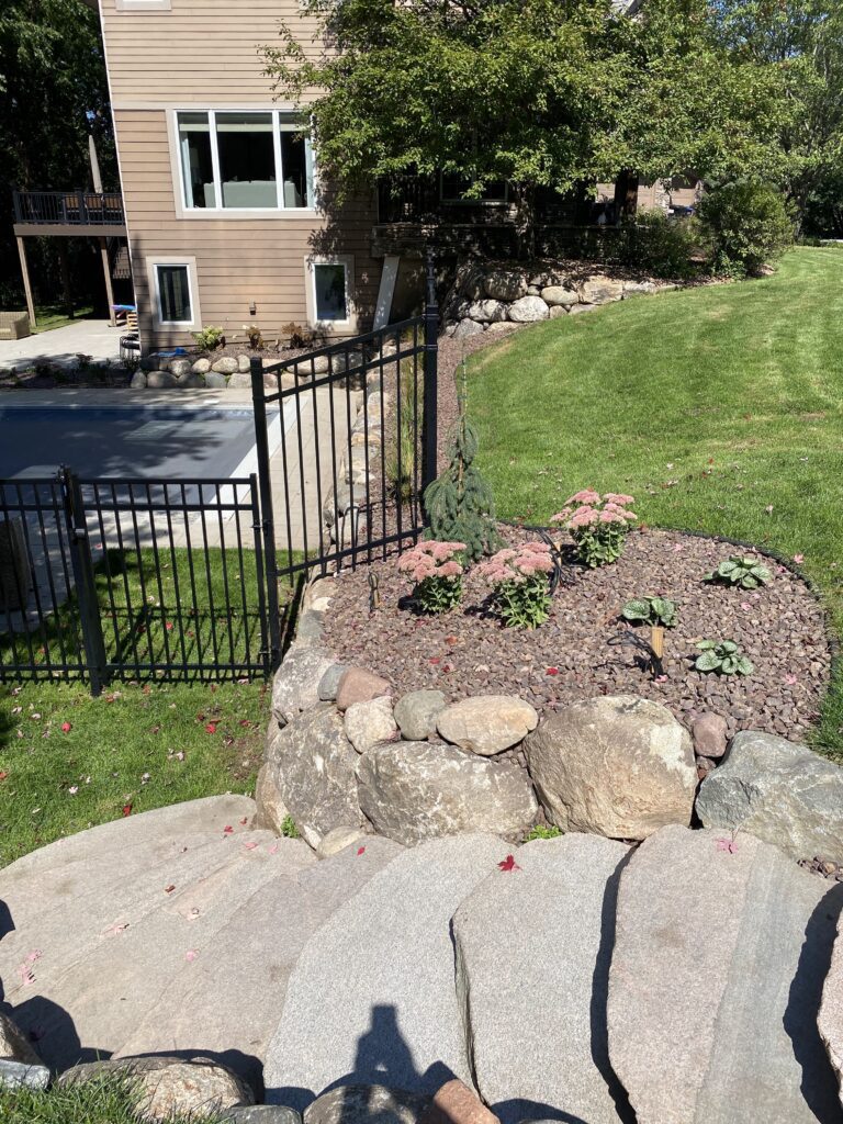 Natural flagstone steps leading down a sloped yard past a heavy boulder retaining wall and black metal safety fence - Yellow Brick Road Pavers & Landscapes LLC