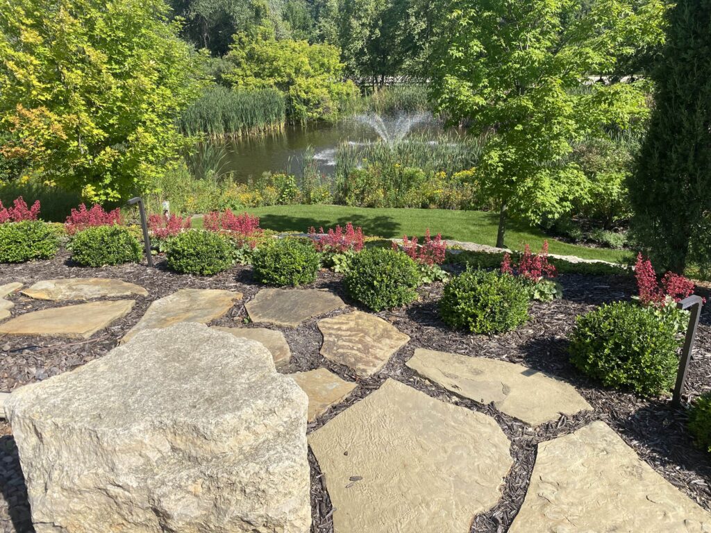Expansive, manicured green lawn and professional landscape beds surrounding a luxury raised stone patio - Yellow Brick Road Pavers & Landscapes LLC