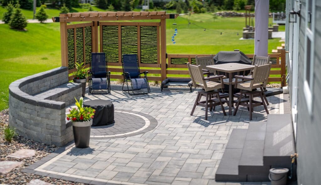 Outdoor patio featuring stone seating, a round dining table, and lounge chairs, surrounded by greenery. Ideal for relaxation and gatherings - Yellow Brick Road Pavers & Landscapes LLC