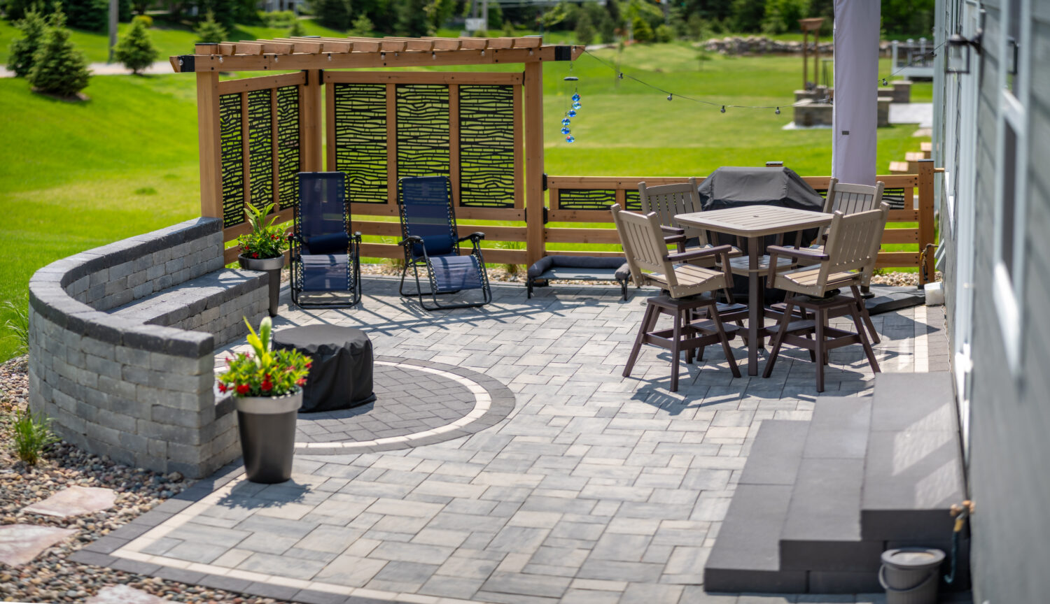 Outdoor patio featuring stone seating, a round dining table, and lounge chairs, surrounded by greenery. Ideal for relaxation and gatherings.