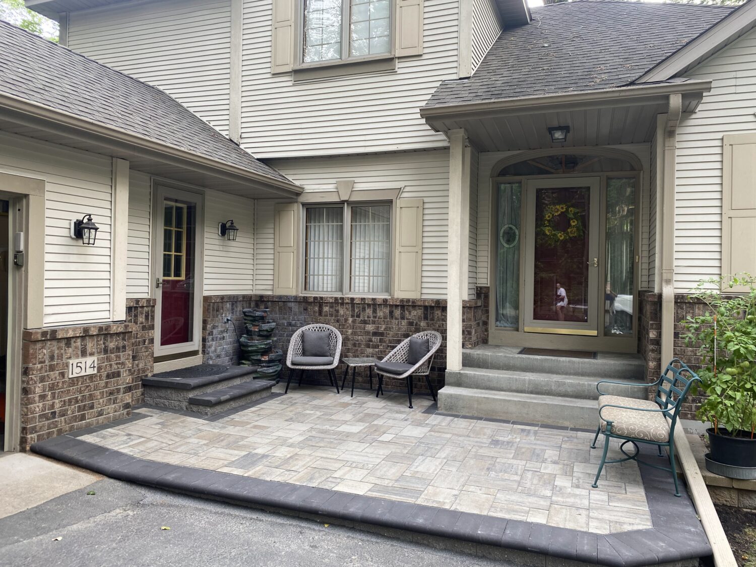 Front porch of a two-story house featuring a welcoming entrance with a glass door, decorative wreath, and modern seating. The area is landscaped with stone accents.