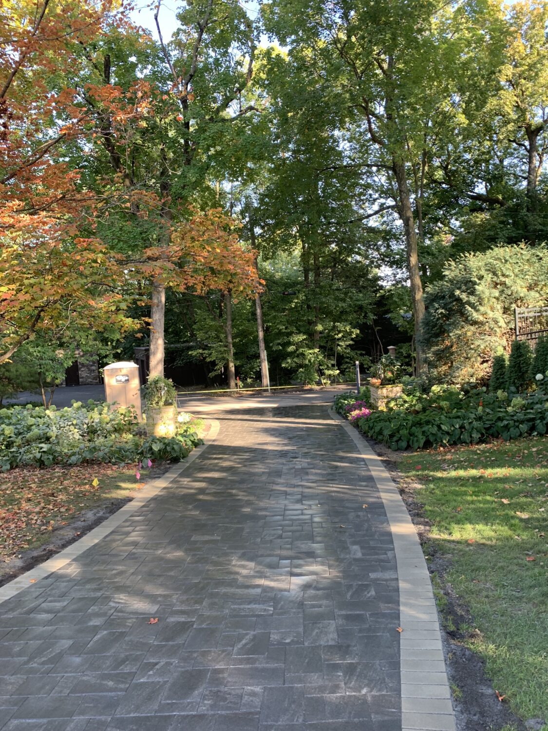 Curved stone pathway lined with autumn-colored trees and lush garden beds, leading through a tranquil landscape.