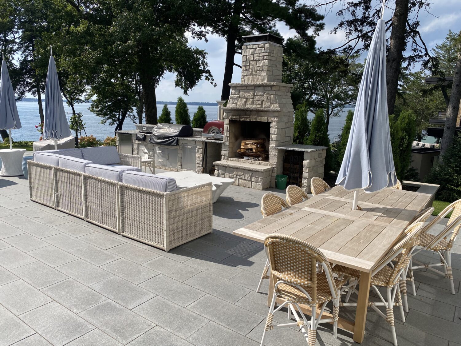Lakeside patio featuring a stone fireplace, a cozy sofa, and a wooden dining table set with chairs, creating a perfect outdoor gathering space.