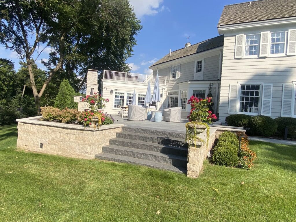 Stylish backyard patio featuring stone steps, colorful flowers, and seating. Ideal for outdoor gatherings, showcasing lush greenery and a modern home.